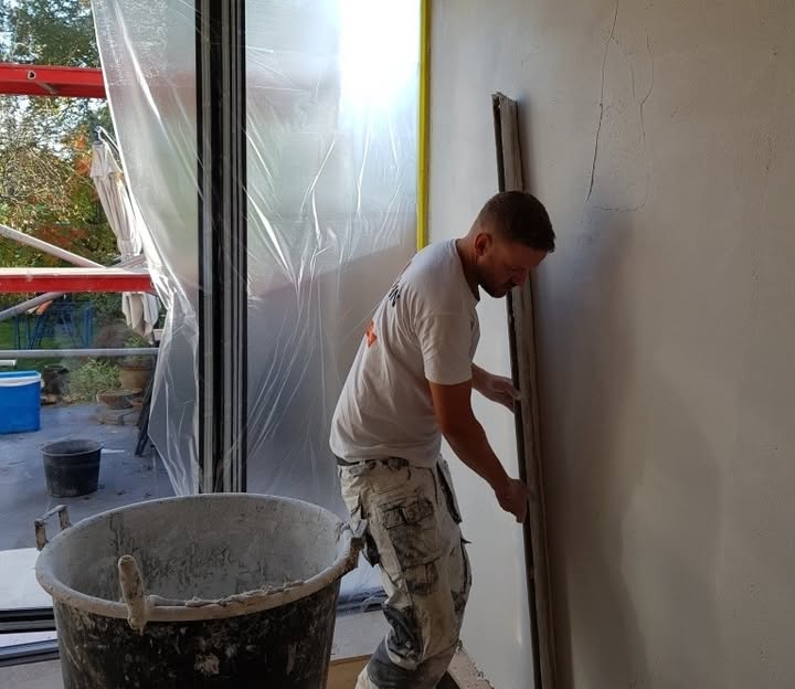 Daan Gertenaar trekt een wand strak met een rei, met een speciekuip op de voorgrond
