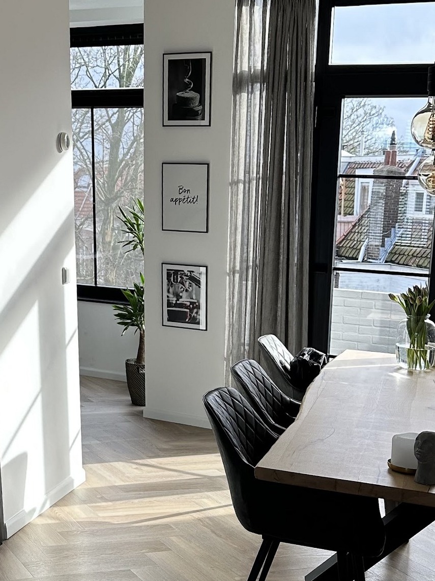 Woonkamer na oplevering: gladde lichte wanden met ingelijste prints, een visgraatvloer en de eettafel bij het raam